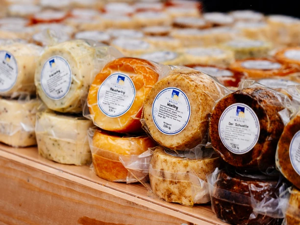 Verschiedene verpackte Käsesorten auf einem Holzregal beim Deutschen Käsemarkt in Nieheim.