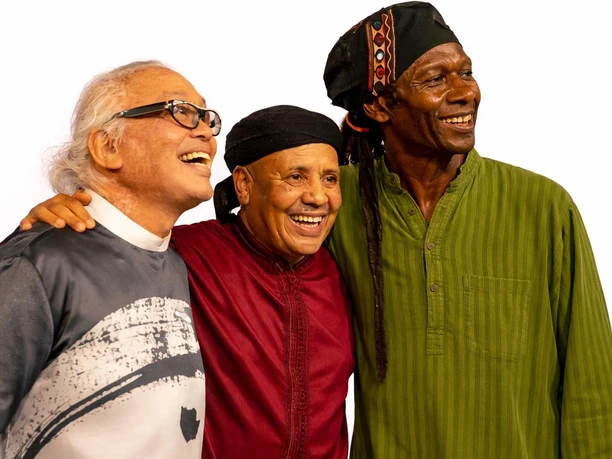 Majid Bekkas, Nguyen Le, and Hamid Drake are smiling together against a light-colored background