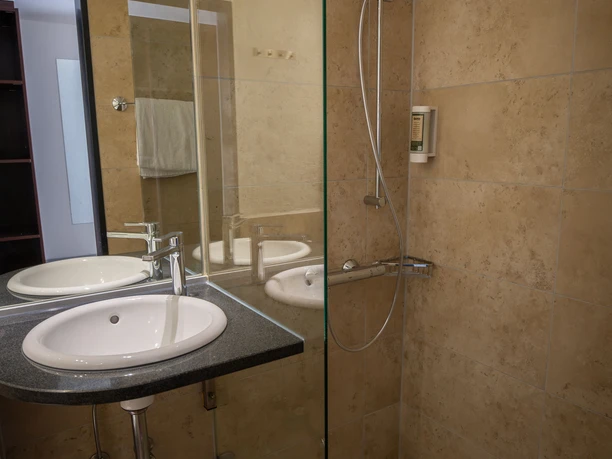 Badezimmer mit beigen Fliesen, weißem Waschbecken und begehbarer Glasdusche.