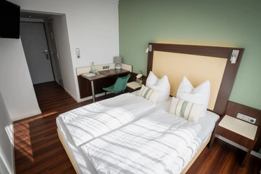 Doppelzimmer im Gästehaus am Räuschenberg mit weißer Bettwäsche und grüner Wand.