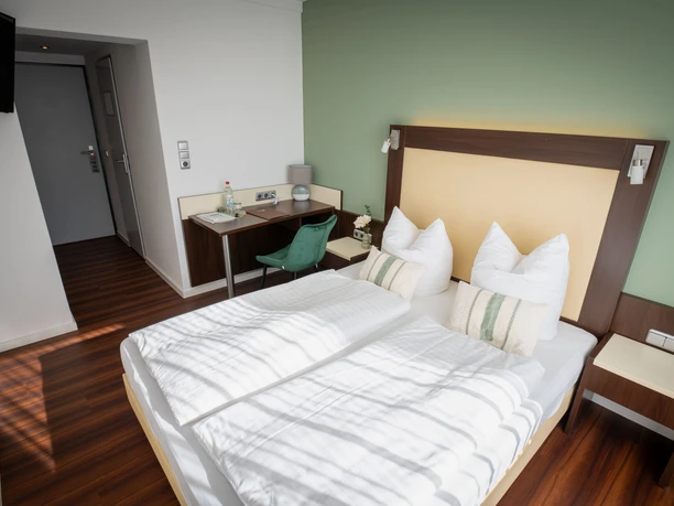 Doppelzimmer im Gästehaus am Räuschenberg mit weißer Bettwäsche und grüner Wand.