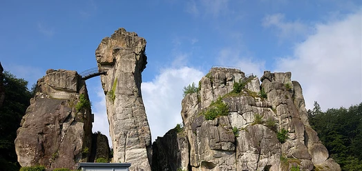 Felsformation der Externsteine mit Brücke vor blauem Himmel und Wald