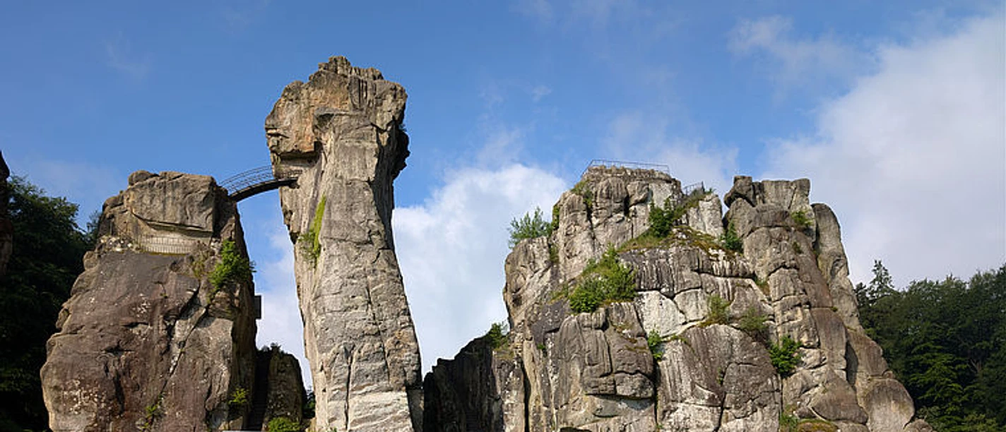 Felsformation der Externsteine mit Brücke vor blauem Himmel und Wald
