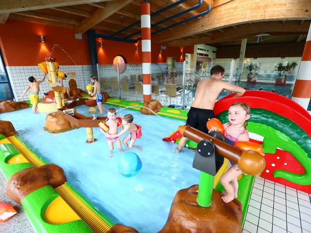 Kinder planschen im Familienbecken mit Wasserspielgeräten und kleiner Rutsche im Plantsch Schongau