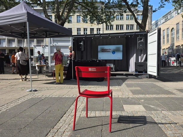 Miteinander NEUmarkt - Cultural Program at Neumarkt Red chair in front of the stage and information booth at the Open-Air Miteinander NEUmarkt in Cologne