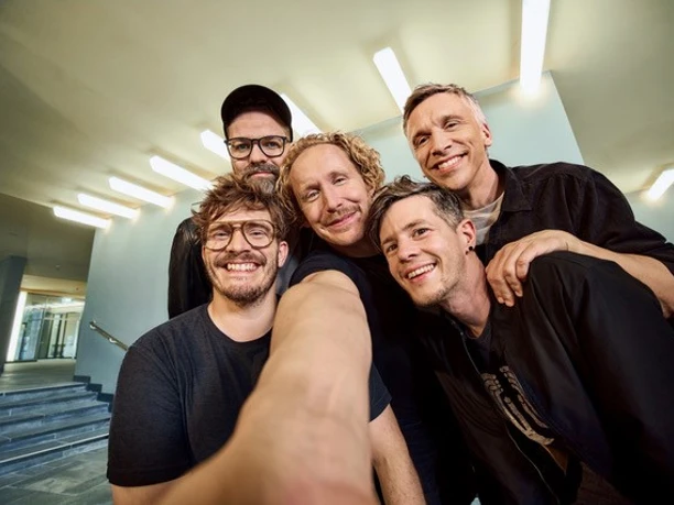 Kasalla Fünf Mitglieder von Kasalla lächeln bei einem Selfie in einem hellen Foyer.