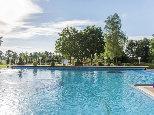 Therme Schwangau Außenbecken Außenbecken der Königlichen Kristall Therme mit Garten, Bäumen und blauem Himmel
