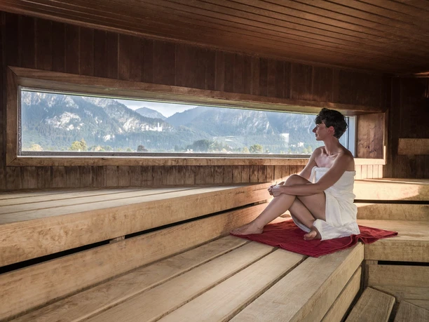 Kristall Therme Schwangau Sauna Saunagast mit Handtuch blickt durch Panoramafenster auf Berge bei Schwangau