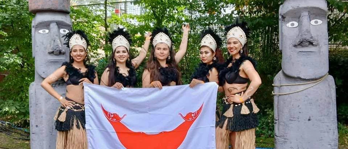 Pehuén e.V. Fünf Tänzerinnen mit Flagge zwischen Moai‑Statuen im Park