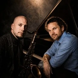 Zwei Jazzmusiker mit Saxofon und Flügel vor dunklem Hintergrund
