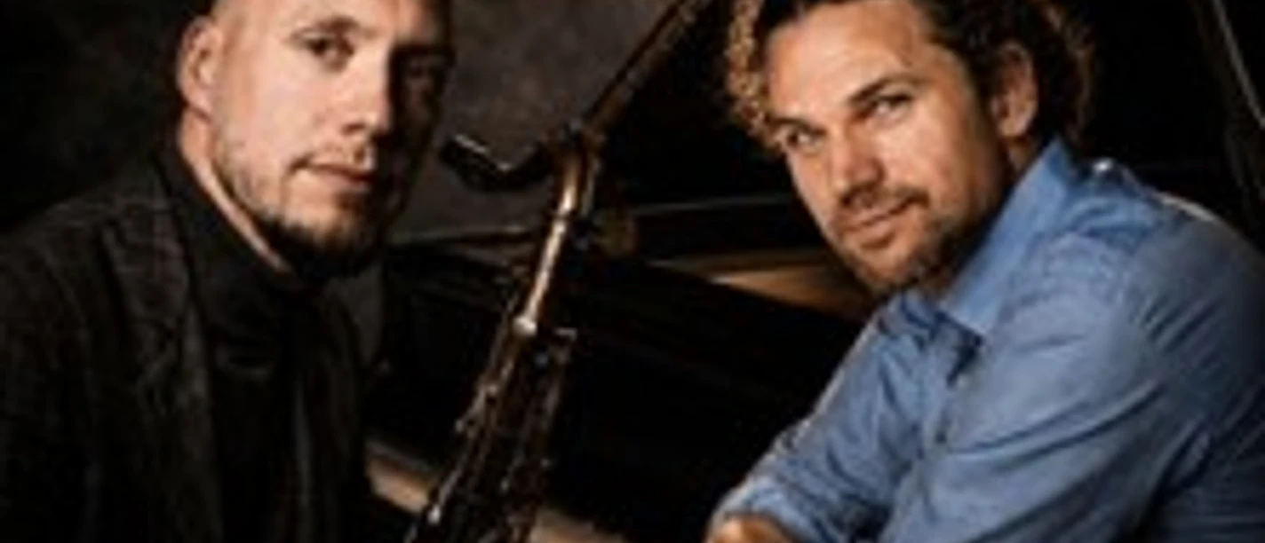 Zwei Jazzmusiker mit Saxofon und Flügel vor dunklem Hintergrund