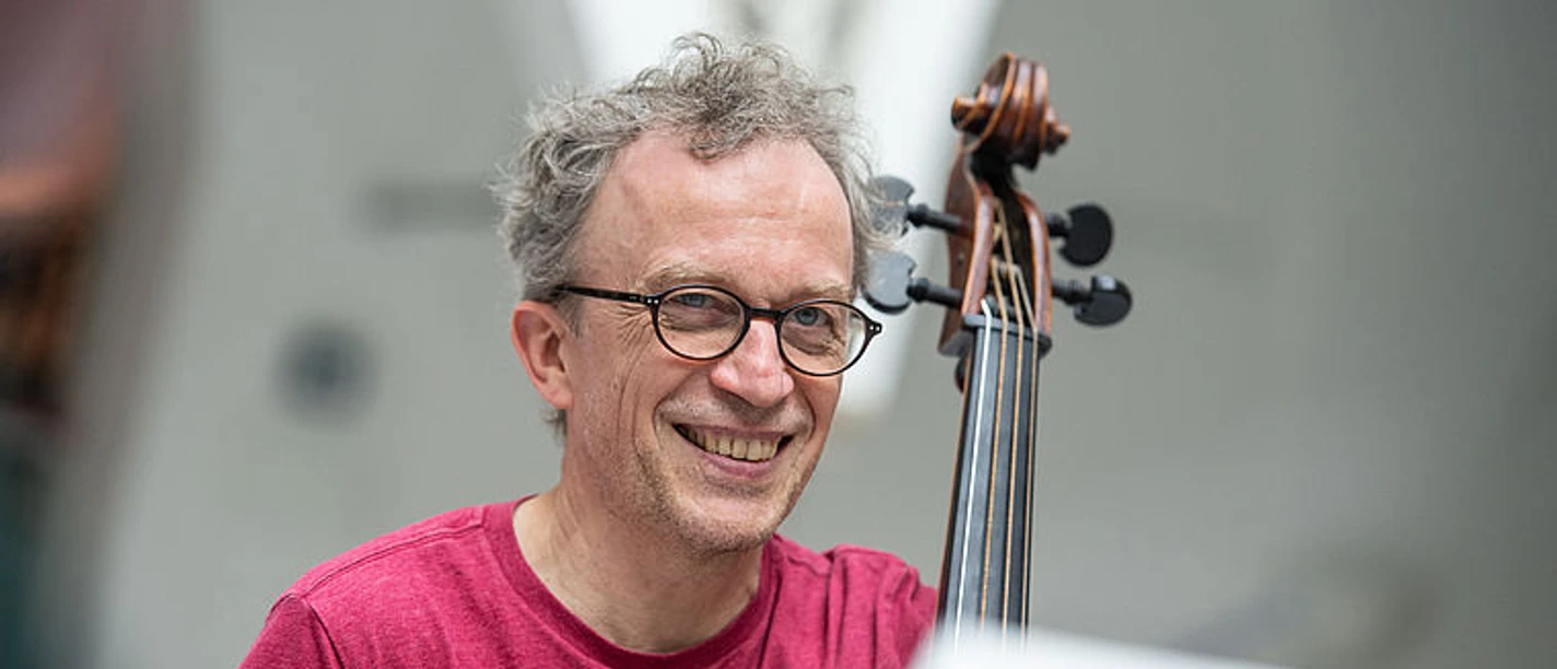 Lächelnder Musiker mit Brille hält ein Streichinstrument in Probenatmosphäre