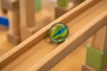 Bunte Glasmurmel auf einer schrägen Holzbahn vor unscharfen Bauklötzen