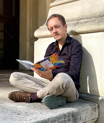 Mann sitzt auf Steinstufen und liest ein buntes Buch über Lebenssinn.
