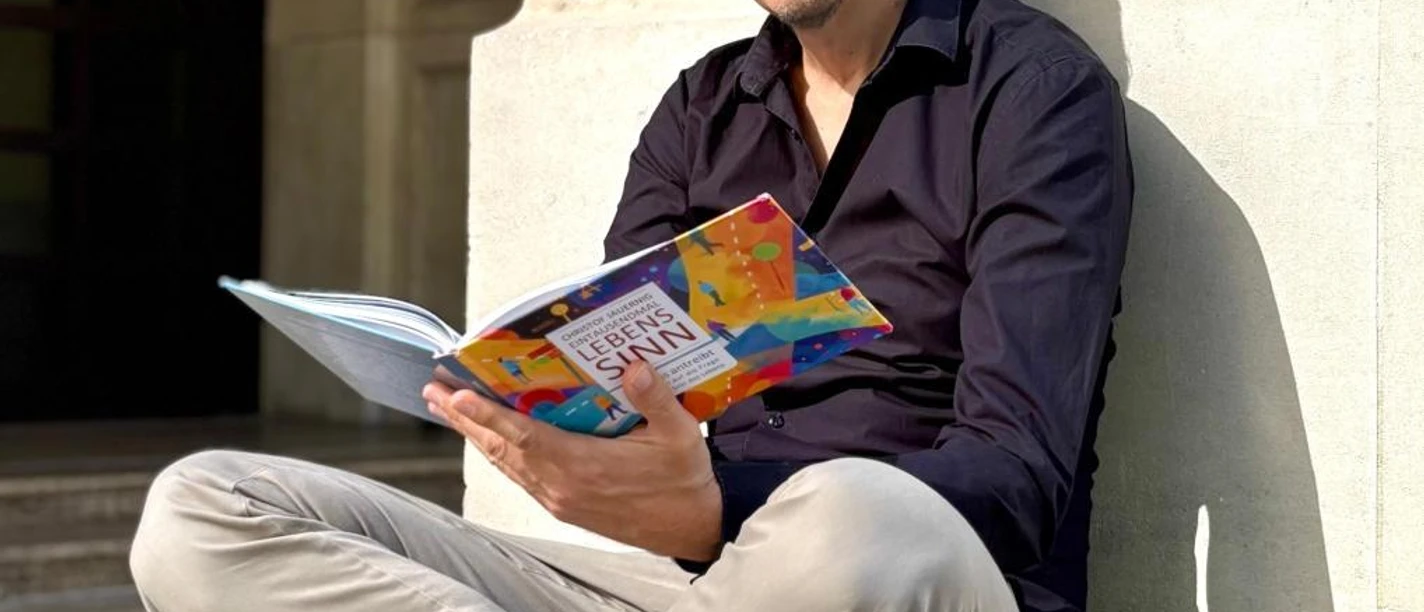Mann sitzt auf Steinstufen und liest ein buntes Buch über Lebenssinn.