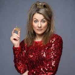 Kathi Wolf in rotem Paillettenkleid mit Krone und Zepter vor grauem Hintergrund