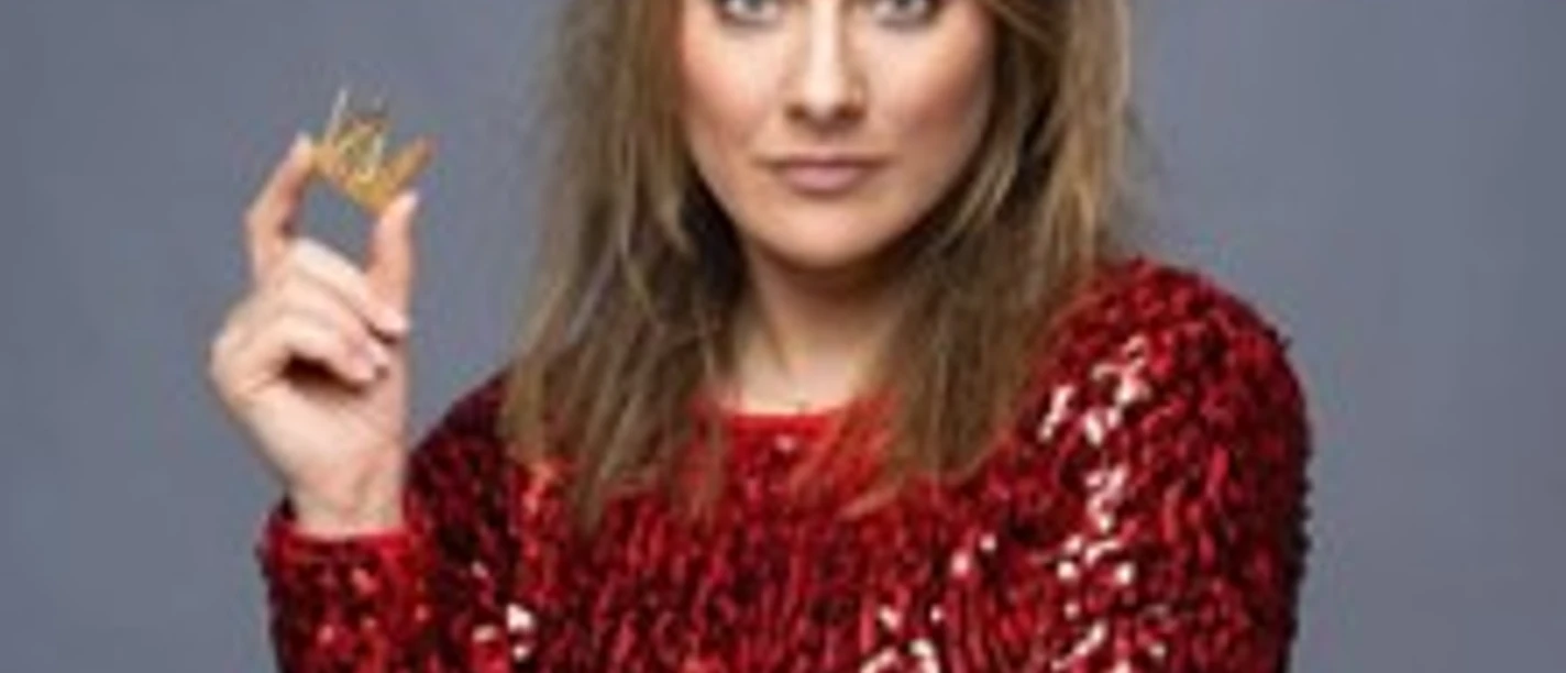 Kathi Wolf in rotem Paillettenkleid mit Krone und Zepter vor grauem Hintergrund