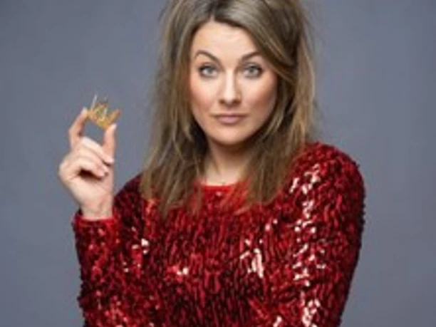 Kathi Wolf in rotem Paillettenkleid mit Krone und Zepter vor grauem Hintergrund