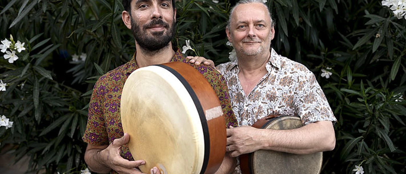 Zwei Musiker mit Rahmentrommeln vor blühenden Sträuchern, Duo Lavoa Lapo.
