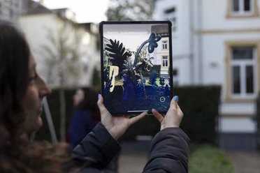 MGGU - Augmented Reality Besucherin nutzt Tablet mit AR‑Ansicht im Museumshof