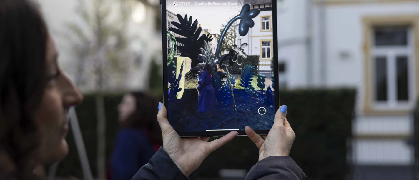 MGGU - Augmented Reality Besucherin nutzt Tablet mit AR‑Ansicht im Museumshof