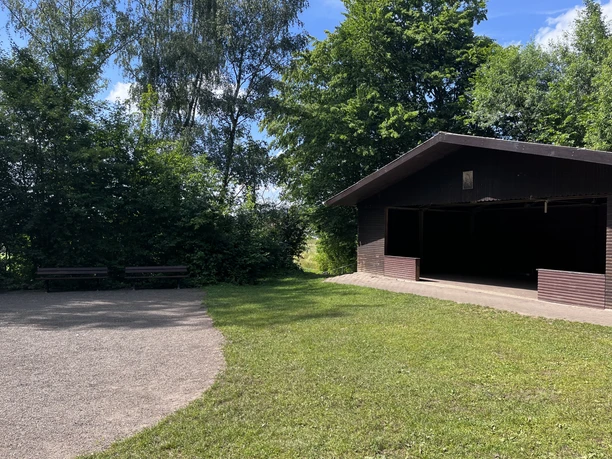 Überdachter Grillplatz mit Bänken auf einer Wiese am Waldrand in Vogelbeck.