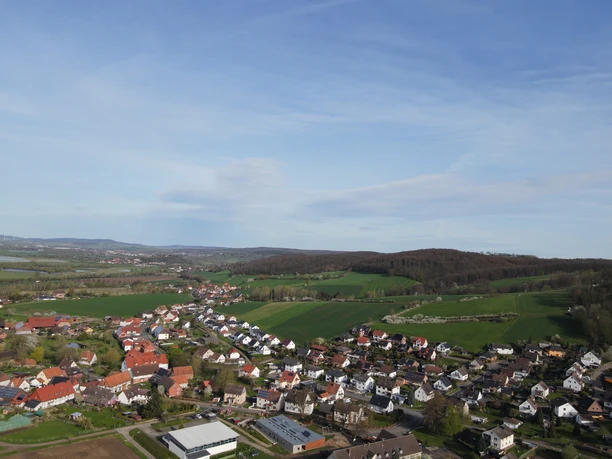 Vogelperspektive auf Vogelbeck mit Häusern, Feldern und bewaldeten Hügeln.