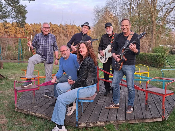 ROCK BUSTER Fünf Musiker mit Gitarren und Mikrofonen auf einer bunten Plattform im Freien.