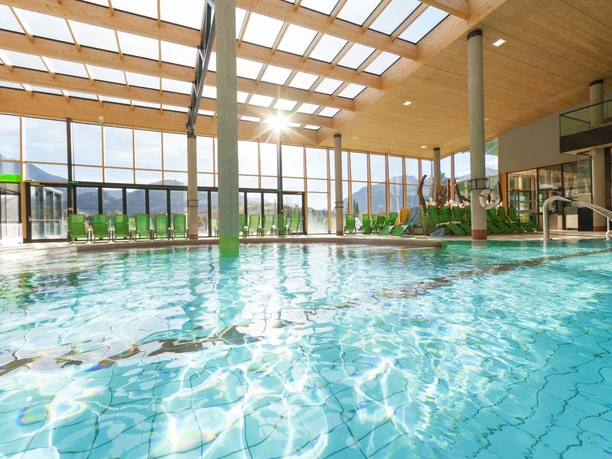 Lichtdurchfluteter Thermenbereich mit Pool, grünen Liegen und Bergblick