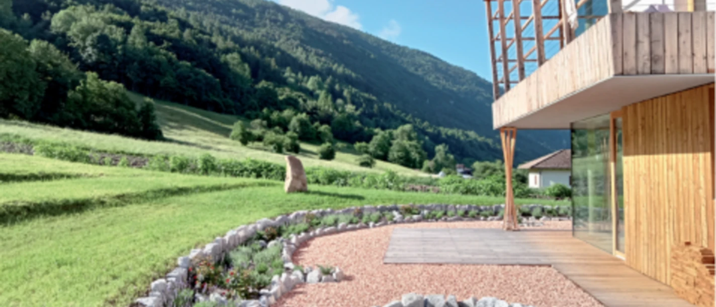 Modernes Holzhaus mit Garten, Steinbeeten und grünen Berghängen im Hintergrund