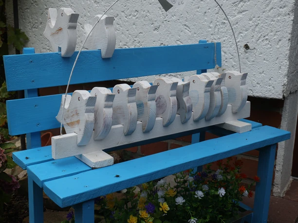 Stockhauser Markt Weiße Holzvögel als Dekoration auf einer blauen Holzbank mit bunten Blumen.