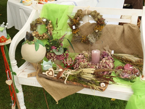 Stockhauser Markt Herbstliche Dekorationen mit Kränzen, Kerzen und einem Kürbis auf einer weißen Holzbank.