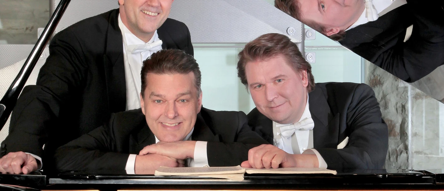 Fünf Musiker im Frack posieren lächelnd an einem geöffneten Flügel.