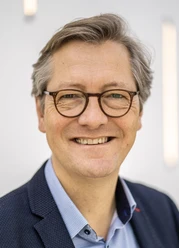 Porträt von Thomas Berning mit Brille, lächelnd vor hellem Hintergrund