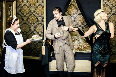 Theaterszene mit Dienstmädchen, elegantem Paar und Teetablett vor goldener Tapete