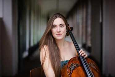 Cellistin Nadège Rochat mit Cello vor unscharfem Innenraumhintergrund