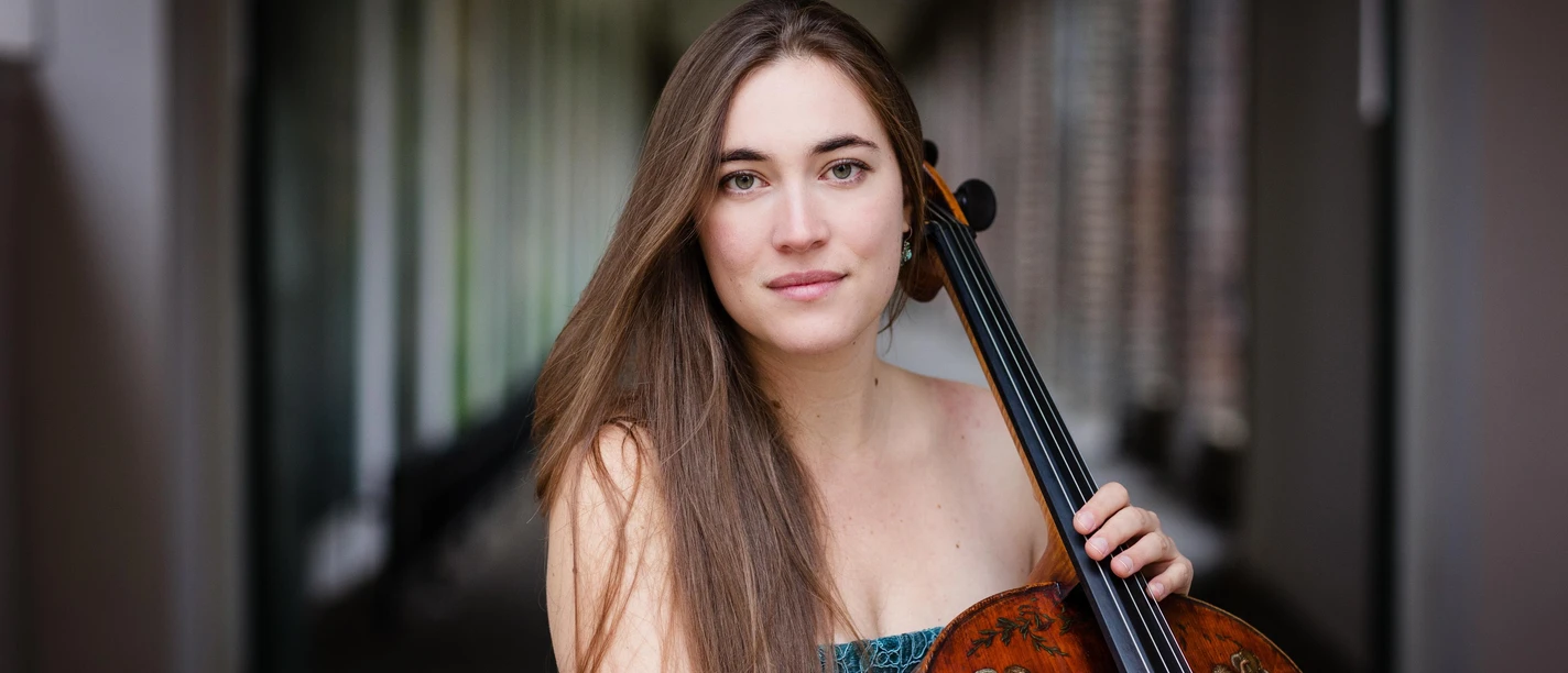 Cellistin Nadège Rochat mit Cello vor unscharfem Innenraumhintergrund
