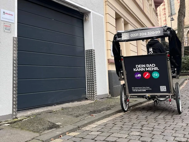 Schwarze Rikolonia-Werkstattrikscha vor der Radwerkstatt in einer Kölner Kopfsteinpflastergasse