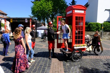 Museum für Kommunikation - Telefonzelle Rote Telefonzelle auf Fahrrad, Personen bei Stadtfest