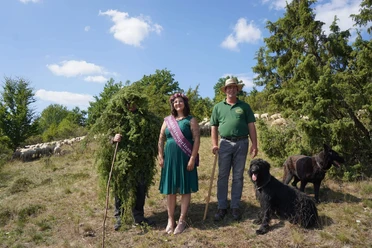 Wacholdermännchen, Heideblütenprinzessin Saija und Schäfer Matthias Bauch stehen mit einem Hund zusammen und freuen sich auf das kommende Heideblütenfest.