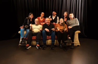 Gruppe sitzt auf Sofa auf Theaterbühne vor Vorhang