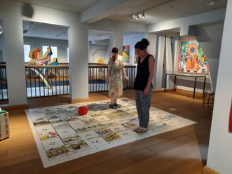 Struwwelpeter Museum - Riesenwürfelspiel Zwei Frauen spielen Bodenspiel mit Würfel im Museum
