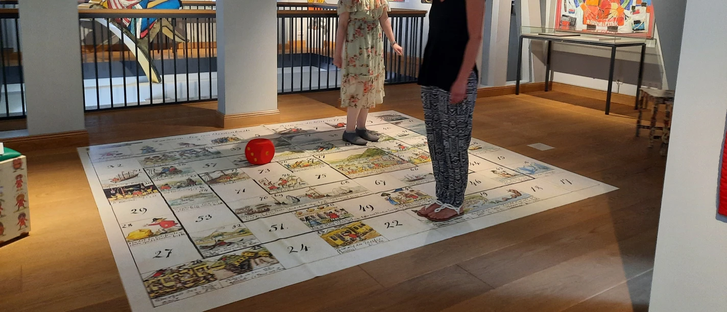 Struwwelpeter Museum - Riesenwürfelspiel Zwei Frauen spielen Bodenspiel mit Würfel im Museum