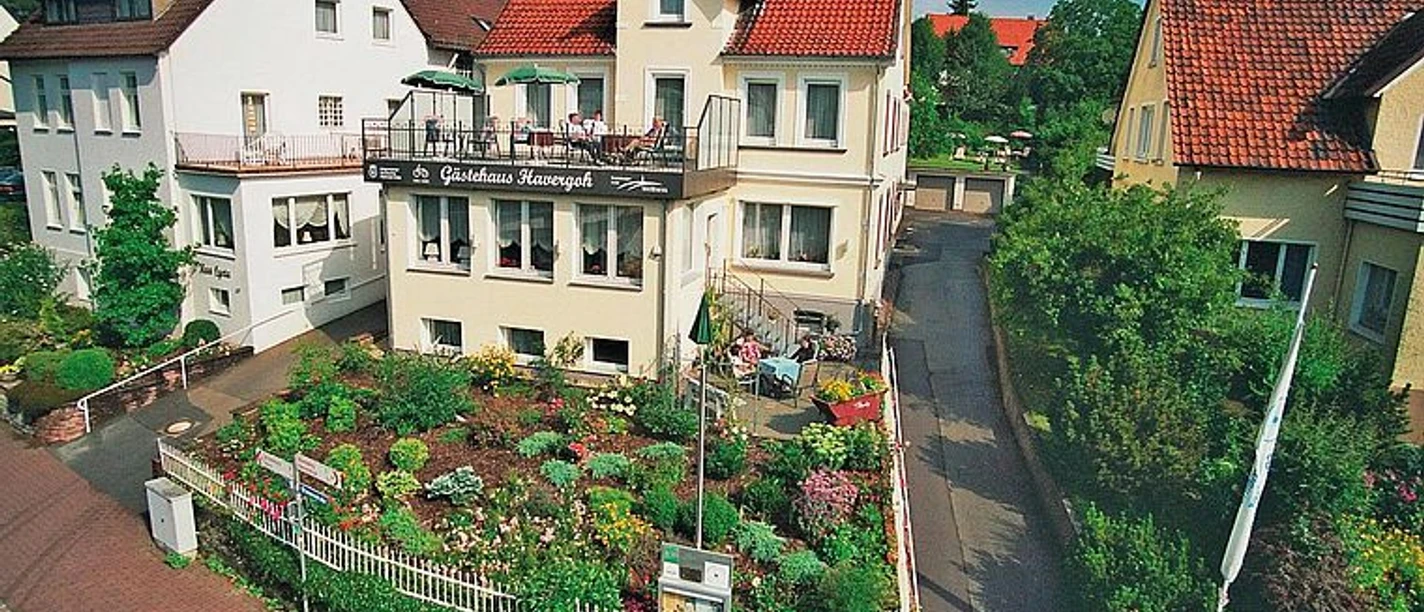 selected_csm_cropmiddle_Bild_Havergoh_06eeb394d6_02.jpg Gasthaus Havergoh mit rotem Dach, Balkon und blühendem Garten an einer ruhigen Straße