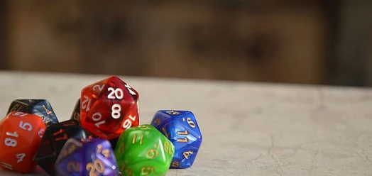 Mehrfarbige Rollenspielwürfel liegen auf einer Tischfläche, der Hintergrund ist unscharf.