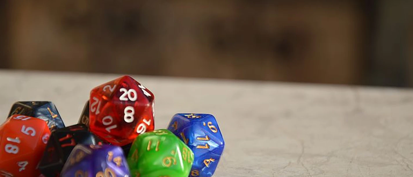 Mehrfarbige Rollenspielwürfel liegen auf einer Tischfläche, der Hintergrund ist unscharf.