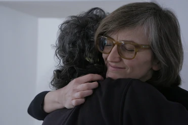zwei Personen umarmen sich, das Gesicht einer Person ist zu sehen, die Person trägt eine Brille und