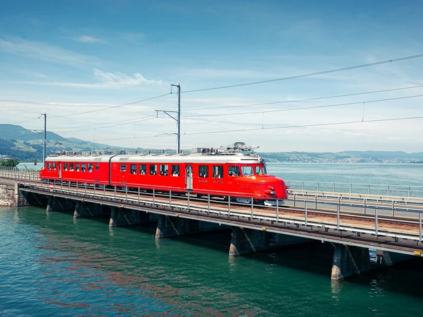 Red SBB charter train crossing a bridge over a Swiss lake with hills in the background