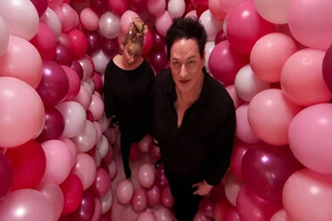 Zwei Musiker in Schwarz stehen zwischen rosa, pinken und weißen Ballons.