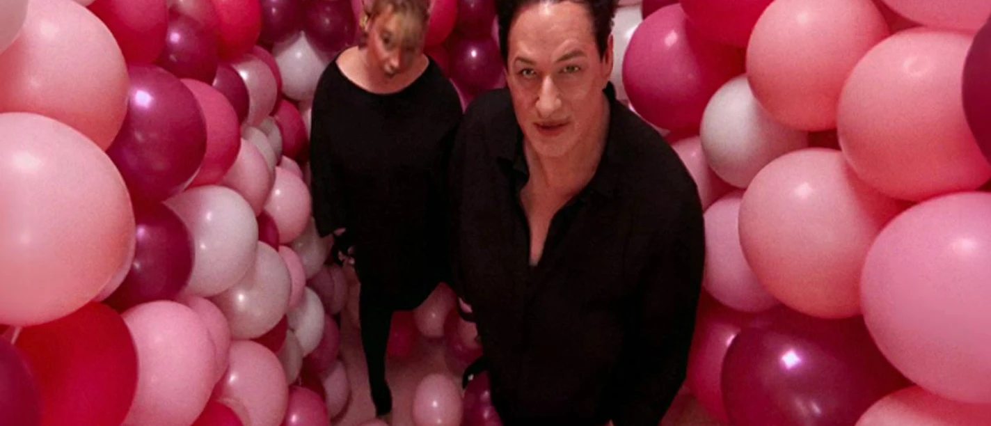 Zwei Musiker in Schwarz stehen zwischen rosa, pinken und weißen Ballons.